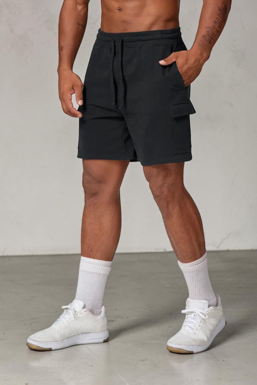 SOLID APPRL black fleece cargo shorts with drawstring waist and side pockets worn by a model in white sneakers.