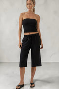 Model wearing a SOLID APPRL black strapless tube top and matching elastic waist wide leg cropped lounge culottes.