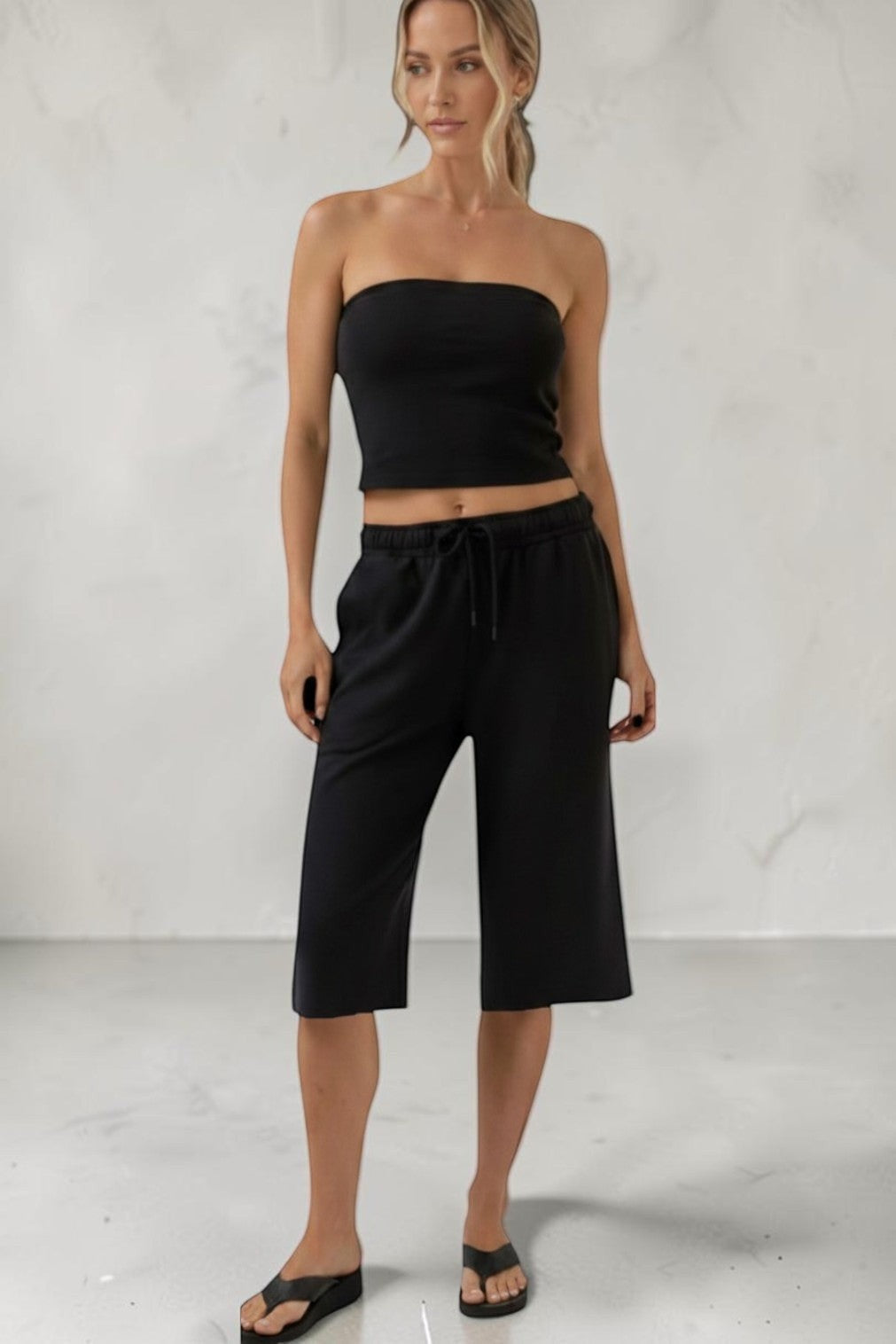 Model wearing a SOLID APPRL black strapless tube top and matching elastic waist wide leg cropped lounge culottes.