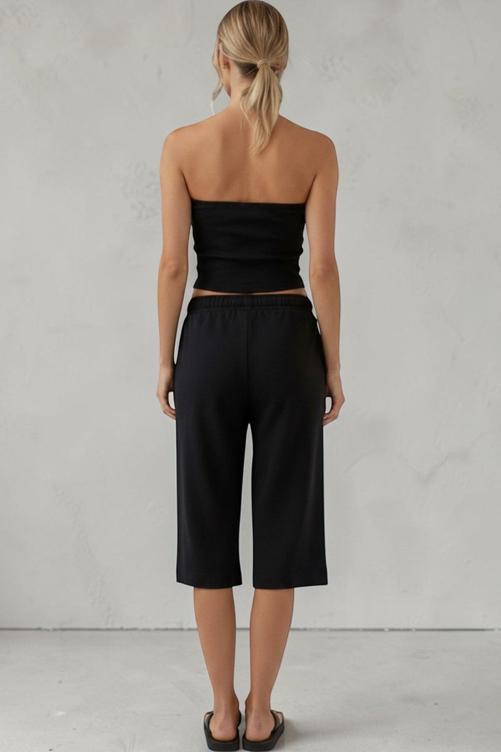 Back view of a woman wearing a SOLID APPRL black strapless tube top and matching elastic waist culotte lounge shorts.