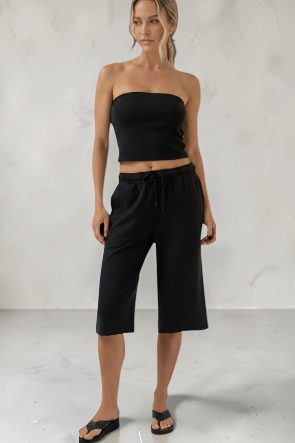 Model wearing a SOLID APPRL black two-piece set with a strapless tube top and cropped wide-leg sweat jorts.
