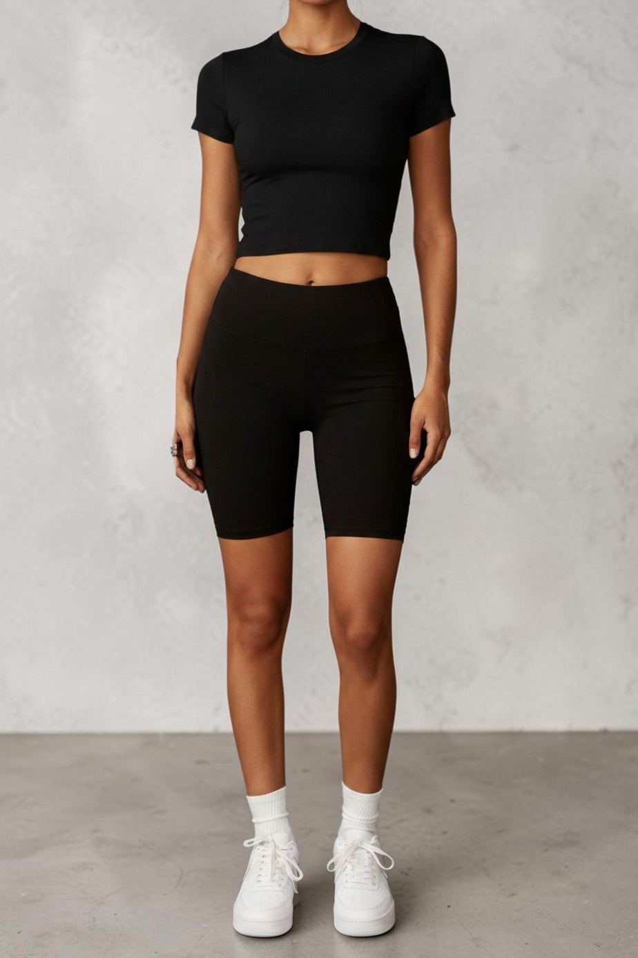 Model wearing a SOLID APPRL off-white short sleeve crew neck crop top and black biker shorts in a minimalist studio.