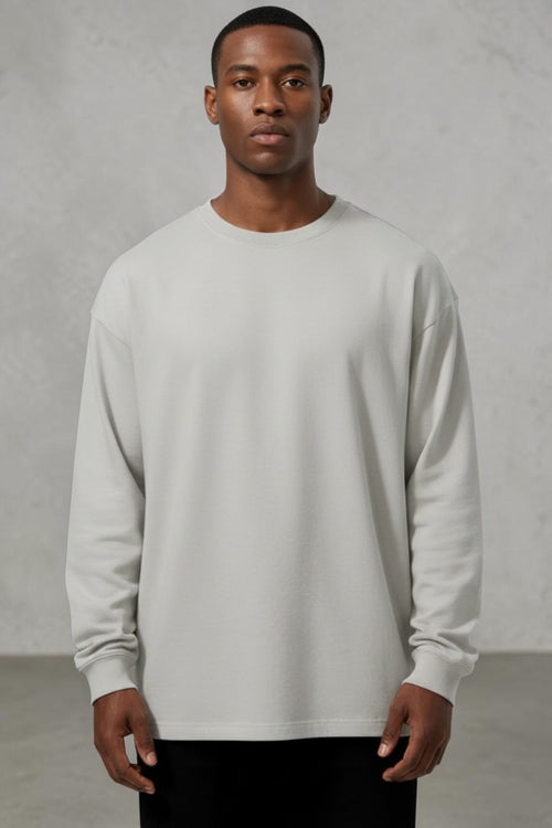 Model wearing a light grey SOLID APPRL long sleeve crewneck shirt with a relaxed fit and ribbed cuffs.