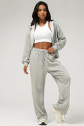Model wearing a SOLID APPRL grey zip-up hoodie and matching wide-leg drawstring lounge pants with a white crop top.