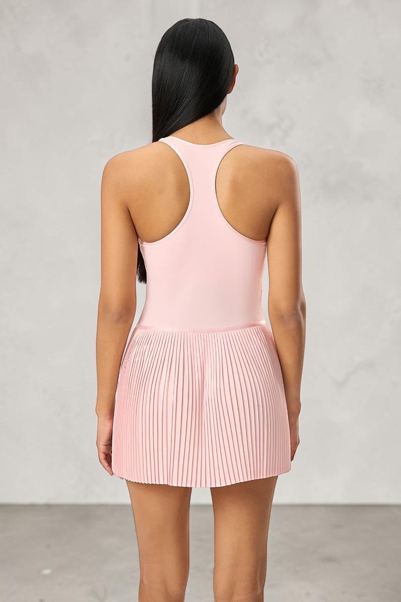 Model wearing a light pink SOLID APPRL pleated athletic tennis dress with a racerback design on a grey background.