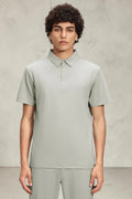 Model wearing a sage green SOLID APPRL short sleeve polo shirt with a structured collar and button placket.